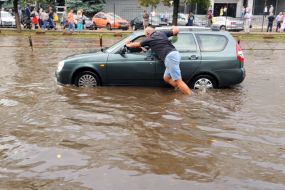 Водитель толкает автомобиль по залитой водой дороге