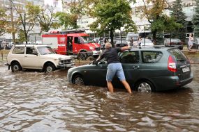 Водитель толкает автомобиль по залитой водой дороге