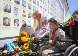 Мальчик в инвалидной коляске кладет букет подсолнухов к Стене памяти