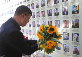 Мужчина кладет букет подсолнухов к Стене памяти