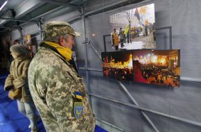 Man with inscription on chevron "Defense of the Maidan" looks at photos