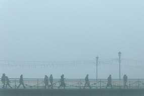 Прохожие идут пешеходным мостом в тумане