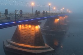 Прохожие идут пешеходным мостом в тумане