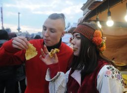 Man and woman in national costumes eat pancakes