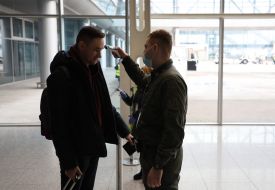 An airport employee checks the temperature of the passenger's body