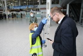 An airport employee checks the temperature of the passenger's body