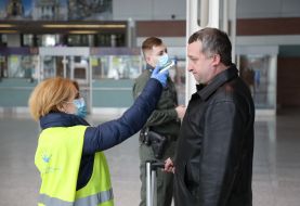 An airport employee checks the temperature of the passenger's body