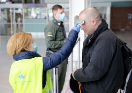 An airport employee checks the temperature of the passenger's body