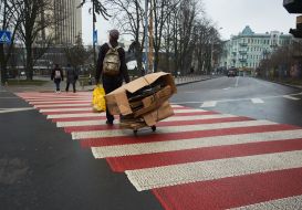 A man carries a cart with waste paper at a pedestrian crossing