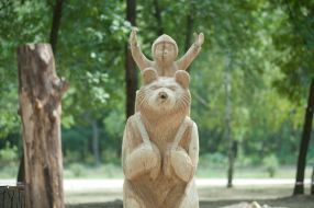 A wooden sculpture of a bear carrying Masha in a basket on his shoulders