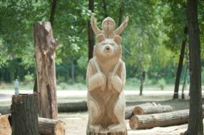 A wooden sculpture of a bear carrying Masha in a basket on his shoulders