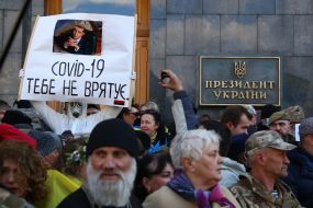 A man in a protective suit holds a poster