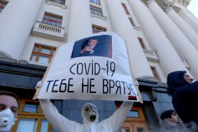 A man in a protective suit holds a poster