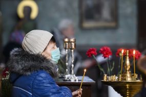 A parishioner in a medical mask puts a candle on a candlestick in the church