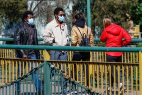 Люди в защитных масках идут по пешеходному мосту