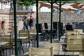 Люди проходят у пустых террас ресторанов