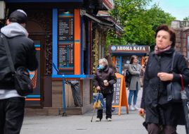An elderly woman in a medical mask asks for alms