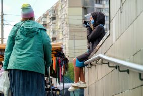 Дівчина в захисній масці сидить біля входу в підземний перехід