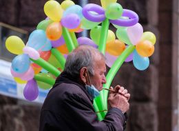 A man in a medical mask carries balloons and lights a cigarette