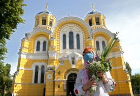 Woman in a medical mask with a bouquet of flowers and grass near St. Vladimir's Cathedral