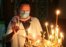 Прихожанка в медицинской маске ставит свечу на подсвечник во Владимирском соборе
