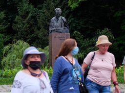 Masked women walk past the monument to Ivan Franko