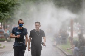 Перехожі проходять біля охолоджувальних рамок, які розбризкують водяний пил