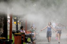 Перехожі проходять біля охолоджувальних рамок, які розбризкують водяний пил