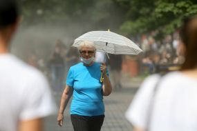 Жінка з парасолькою проходить біля охолоджувальних рамок, які розбризкують водяний пил