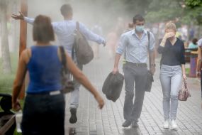 Перехожі проходять біля охолоджувальних рамок, які розбризкують водяний пил