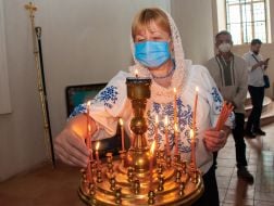 A parishioner in a medical mask puts a candle on a candlestick in the church of St. John the Theologian