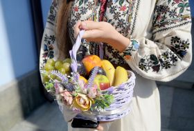 The girl in an embroidered shirt is holding a fruit basket