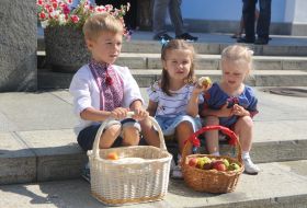 Children in embroidered shirts sit near fruit baskets