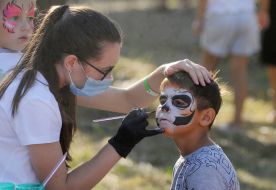 Дівчина в масці розмальовує хлопчику обличчя фарбами