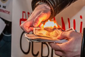 Мужчина поджигает символические бумажные деньги