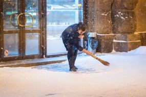 Woman sweeps the snow on the street with a broom