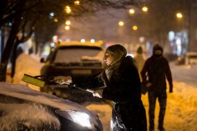 Woman cleans the car from snow
