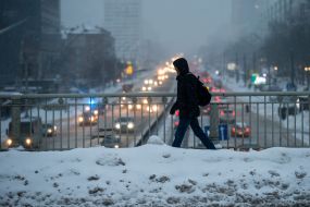 A man walks on a snow-covered bridge over the road