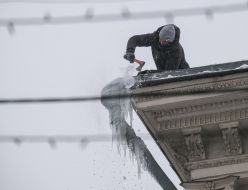 Utility workers knock icicles off the roof of a building