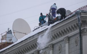Utility workers knock icicles off the roof of a building