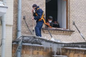 Utility workers knock icicles off the roof of a building