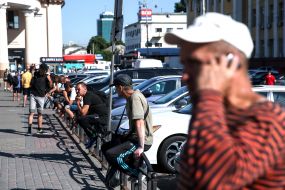 People sit on a pedestrian fence near the road
