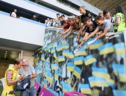 Футболист подписывает футболку возле трибуны с болельщиками