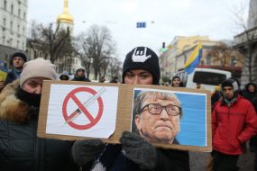 Portrait of Bill Gates and a poster with a crossed syringe in his hands at the rally