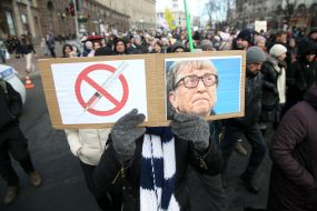 Portrait of Bill Gates and a poster with a crossed syringe in his hands at the rally