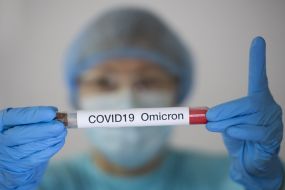 A woman in a protective suit and mask demonstrates a test tube