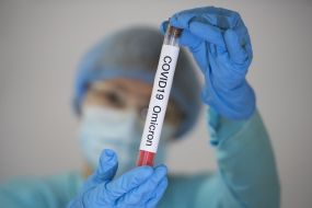 A woman in a protective suit and mask demonstrates a test tube