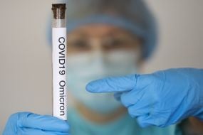 A woman in a protective suit and mask demonstrates a test tube