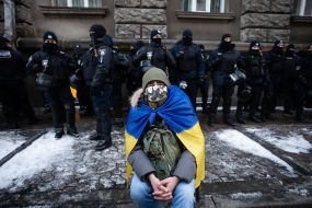 A man with the flag of Ukraine on his shoulders and law enforcement officers