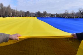 Protesters hold an unfurled flag of Ukraine